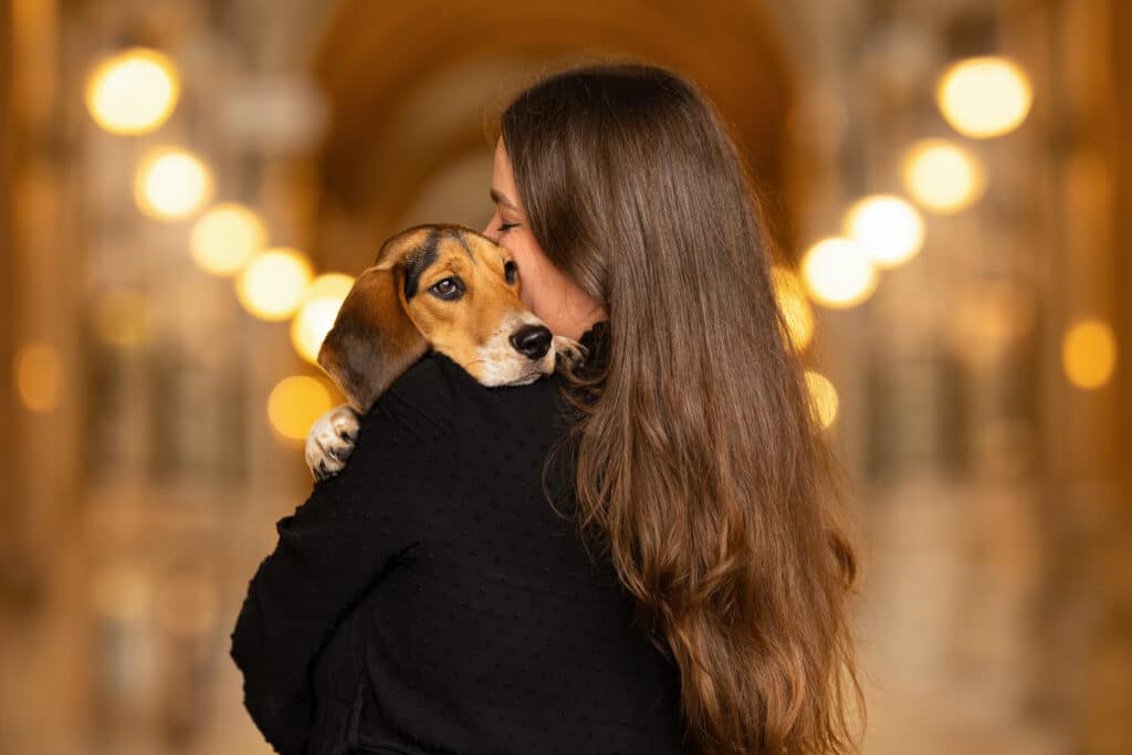 Frau in schwarzer Weste und mit langen braunen Haaren umarmt ihren Beagle